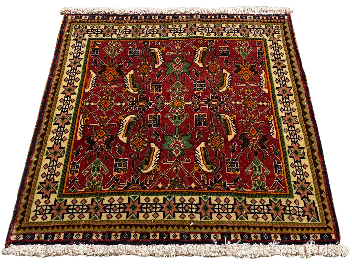 Tapis persan 63x61 cm, vue en biais : motif ornemental rouge sur fond vert et beige.