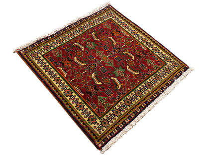 Tapis Poshti 63x61 cm, vue en diagonale : motif rouge avec des détails verts, franges.