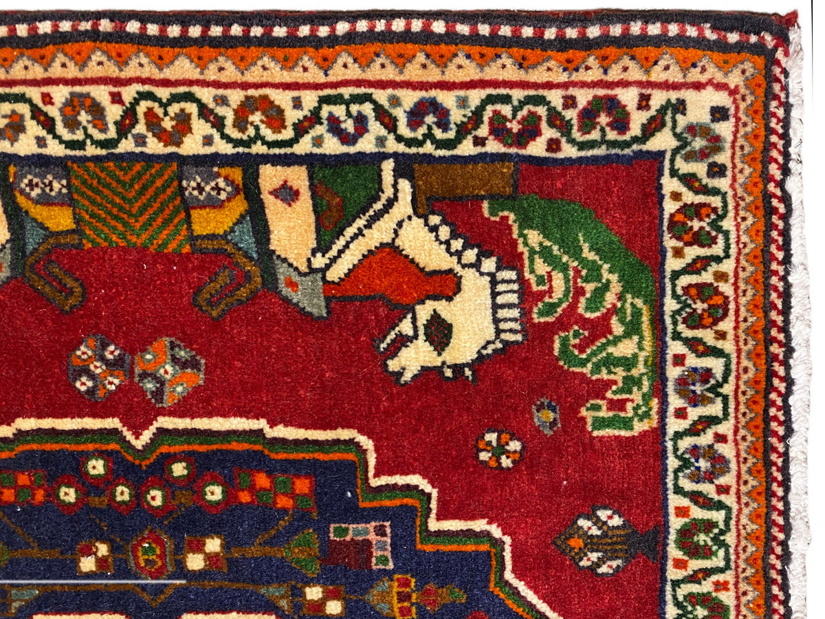 Gros plan sur un tapis Poshti, champ rouge avec des animaux, bordure décorative bleue et frise à motifs