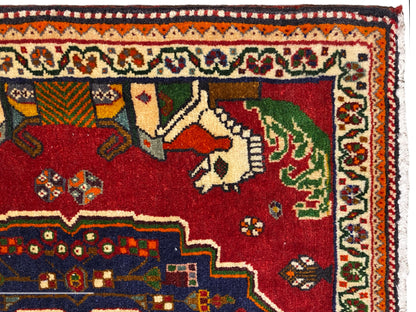 Gros plan sur un tapis Poshti, champ rouge avec des animaux, bordure décorative bleue et frise à motifs