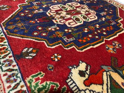 Gros plan d’un tapis Poshti, champ rouge avec une couronne ornementale bleue et des motifs animaliers