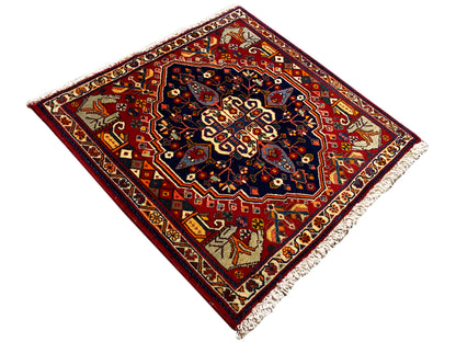 Tapis en composition diagonale : cadre rouge avec centre bleu, motifs d’angle et franges