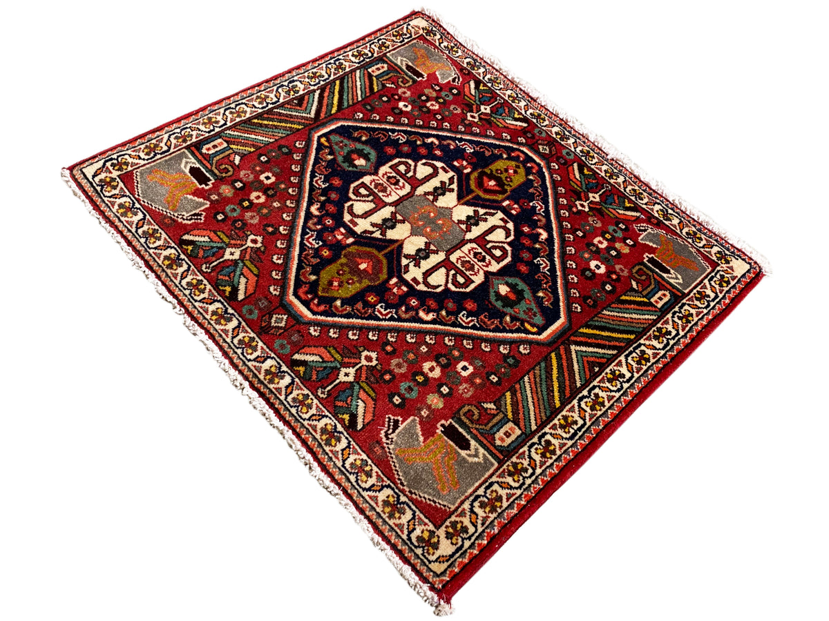 Tapis oriental à fond rouge, motifs couleur crème et bandes décoratives colorées