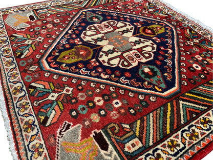 Tapis oriental photographié en biais : motif rouge, médaillon sombre et bordures multicolores