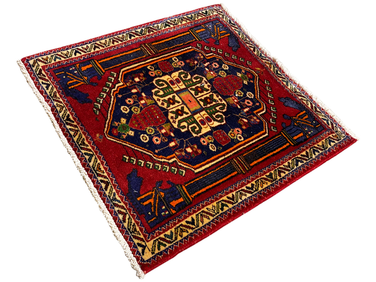 Tapis Poshti 66x62 cm en diagonale : bordure bleu-rouge ornée de nombreux motifs.