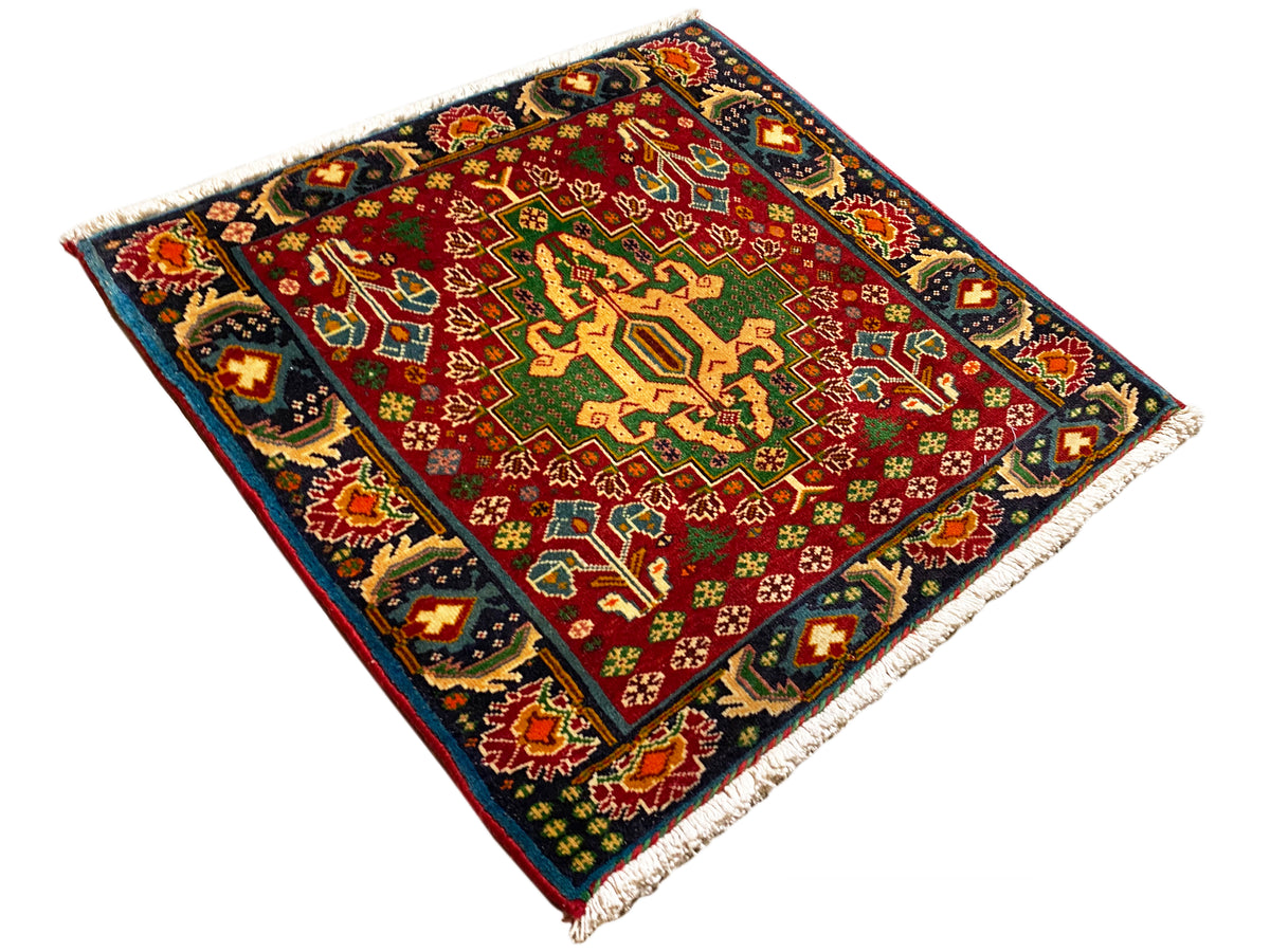 Tapis rectangulaire (67x66 cm) photographié en diagonale ; champ rouge, bordure sombre, franges