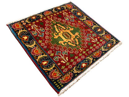 Tapis rectangulaire (67x66 cm) photographié en diagonale ; champ rouge, bordure sombre, franges