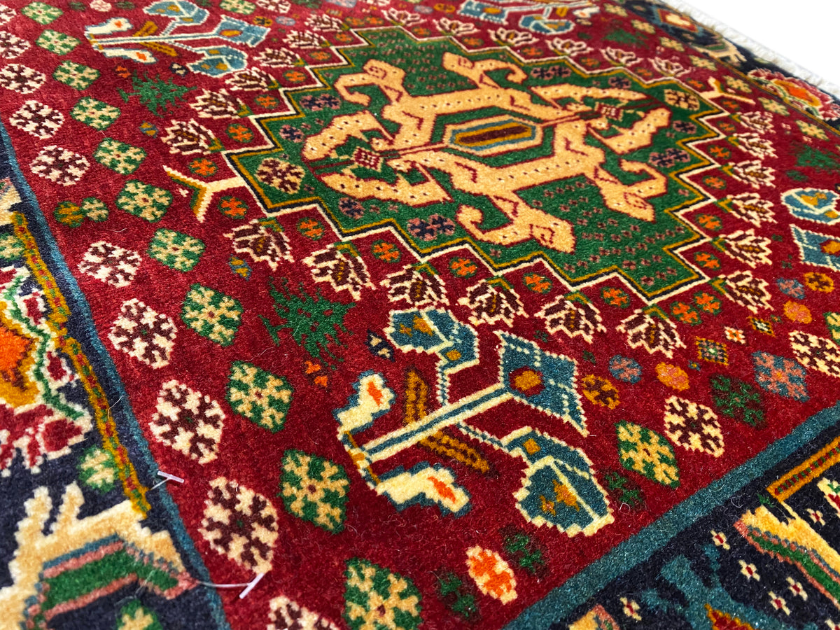 Détail de la face avant d’un tapis avec un champ rouge, des motifs en forme d’étoiles et des lignes turquoise, avec un velours texturé