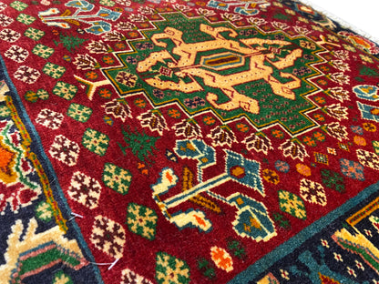 Détail de la face avant d’un tapis avec un champ rouge, des motifs en forme d’étoiles et des lignes turquoise, avec un velours texturé