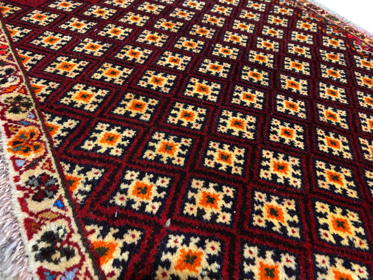 Tapis Poshti 61x59 cm : gros plan du motif avec des losanges colorés sur fond rouge foncé