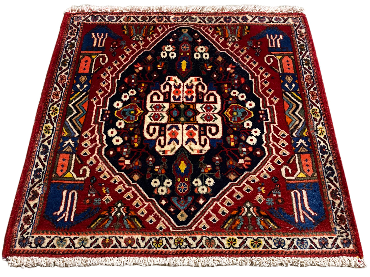 Tapis à bord rouge, centre bleu foncé et ornements multicolores, franges