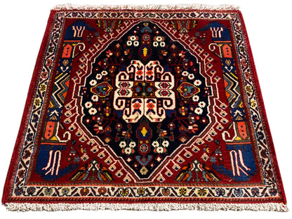 Tapis à bord rouge, centre bleu foncé et ornements multicolores, franges