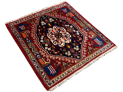 Tapis d’apparence carrée à fond rouge, médaillon central bleu foncé et franges