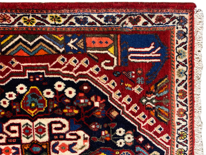Vue détaillée du tapis : fond rouge, champ bleu foncé, ornements et bordure