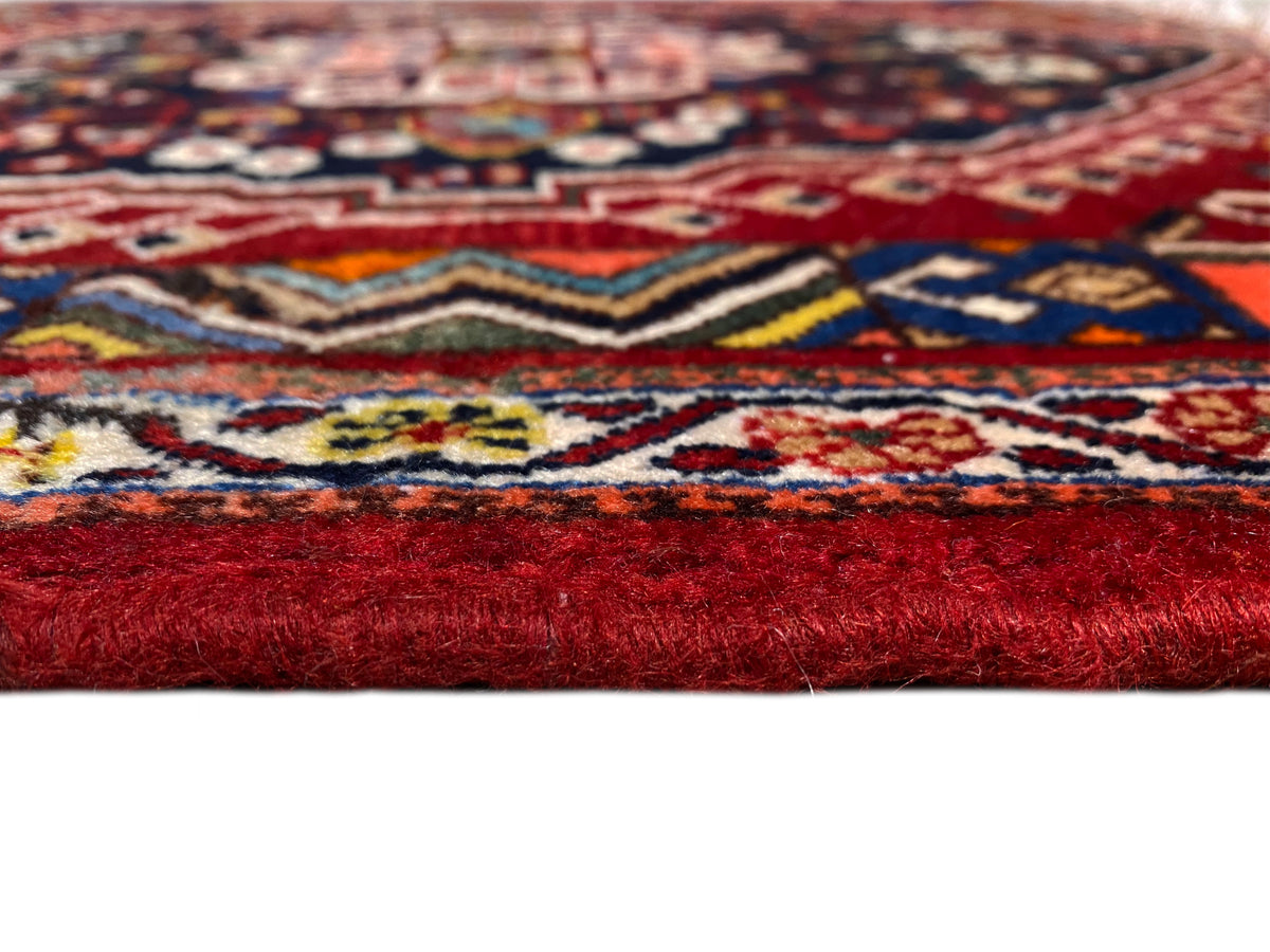 Détail de tapis avec un motif coloré et des fibres rouges hautes sur le bord