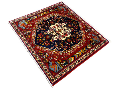 Tapis Poshti 65x61 cm, vue en diagonale : champ rouge avec motif sombre et ornements de bordure