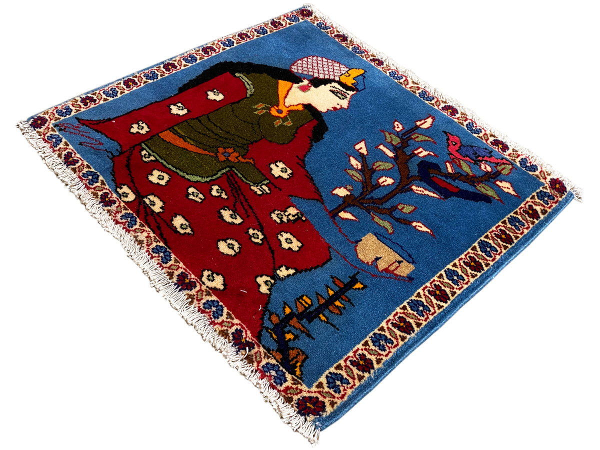 Tapis Poshti 65x63 cm vu de biais, personnage, vêtement rouge et ornements bleus